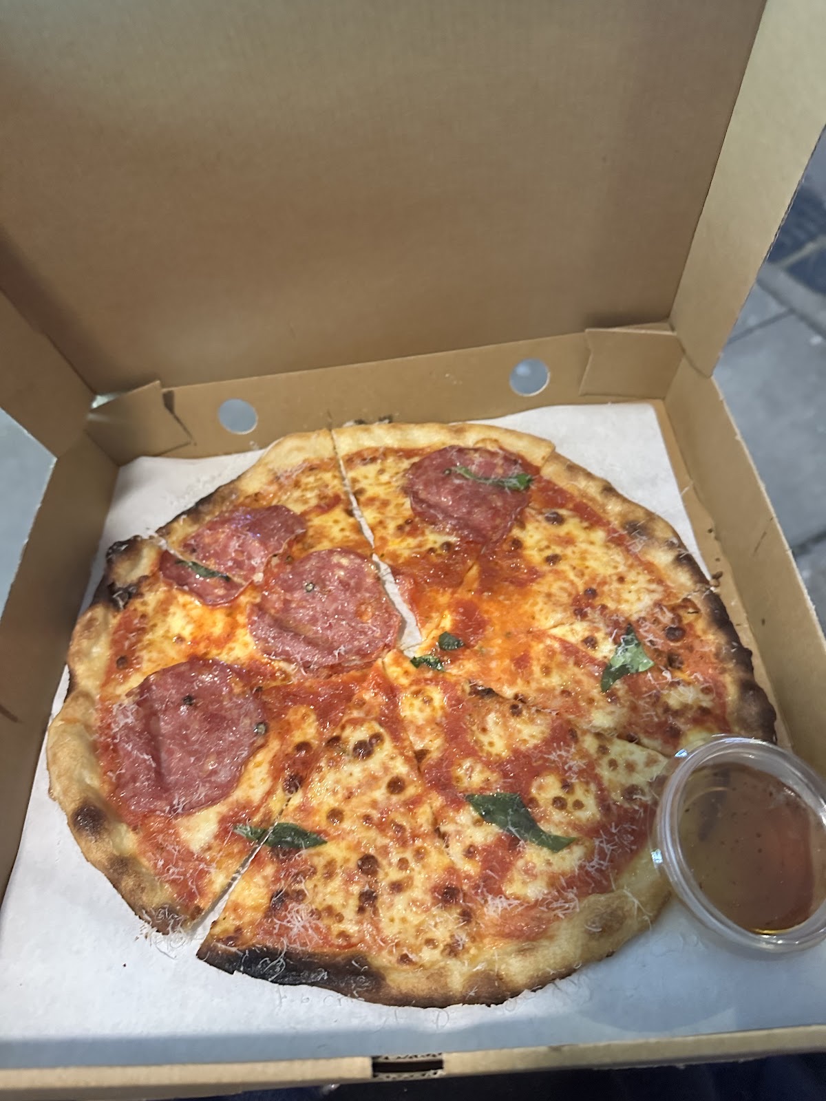 A half-pepperoni pizza in an open takeaway box with a pot of dip