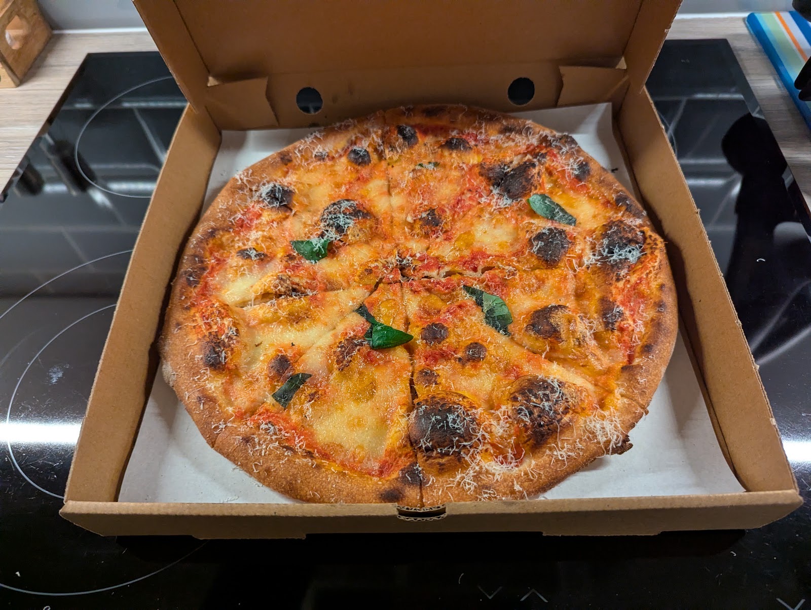 A margherita pizza in an open box, fresh out of the kitchen